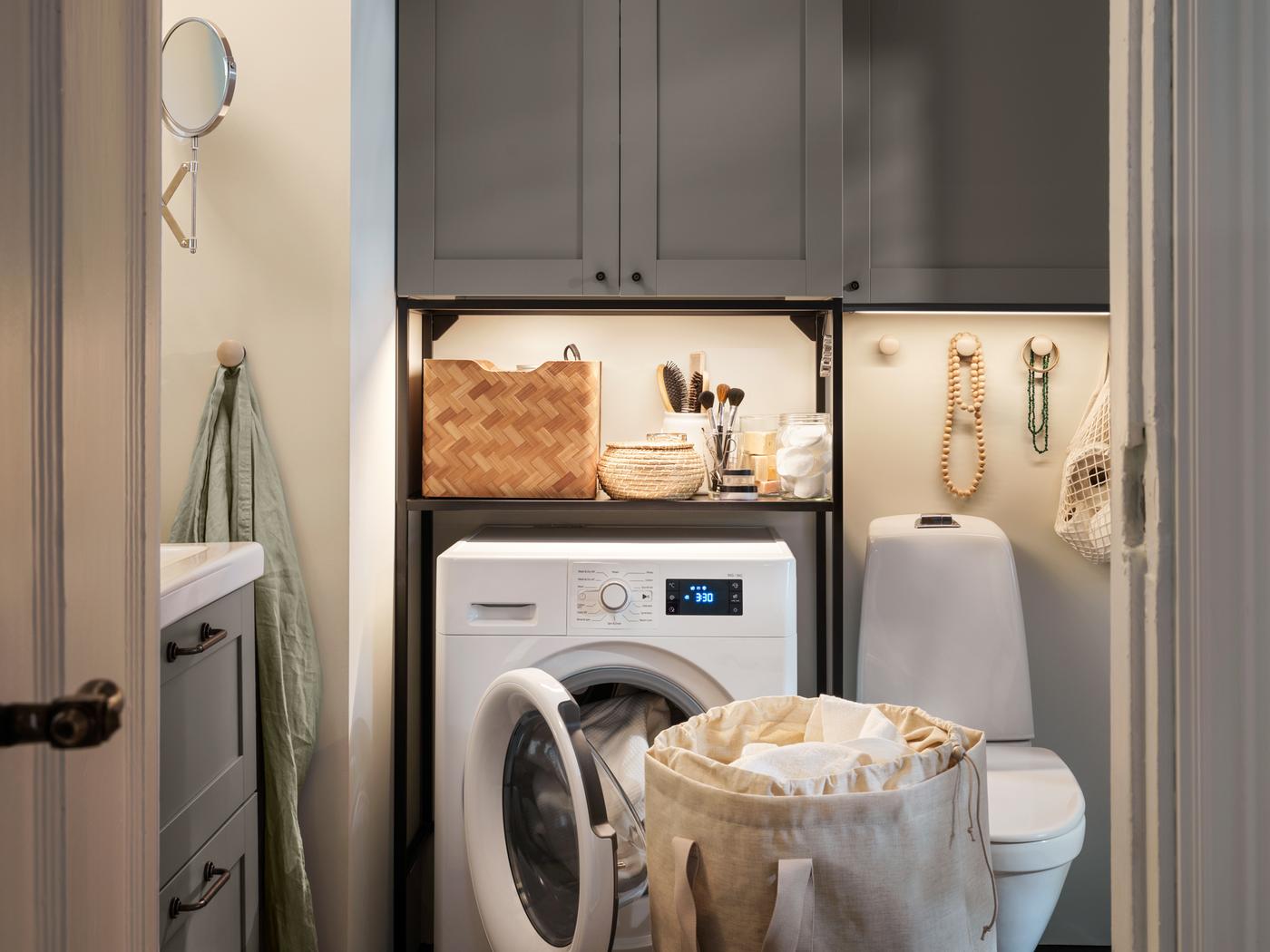 Pralnica v kopalnici, rešitev za shranjevanje s sivimi ENHET ličnicami, UDDARP pralno-sušilni stroj in PURRPINGLA vreča za perilo.