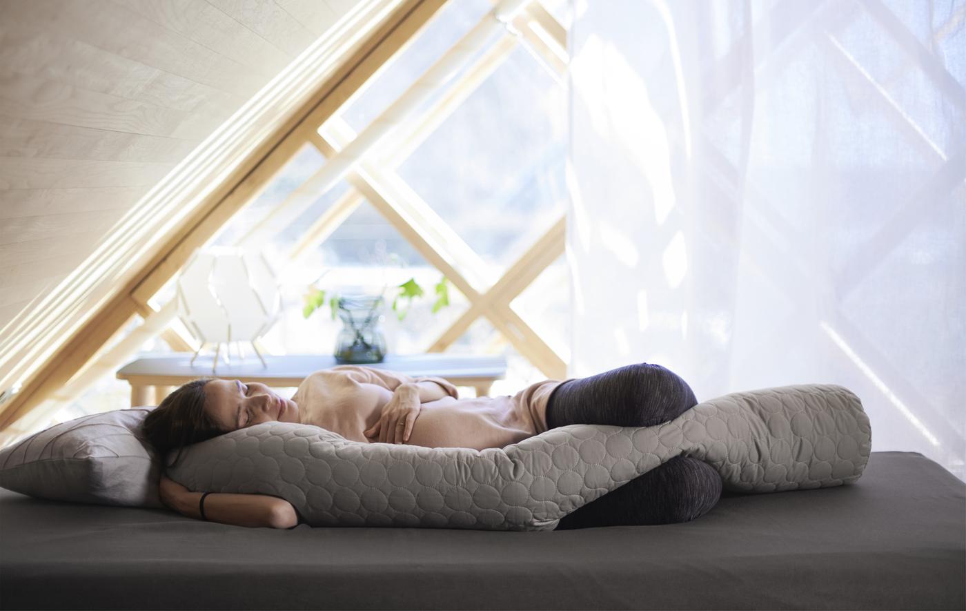 Pregnant woman sleeping on bed with a body-length cushion.