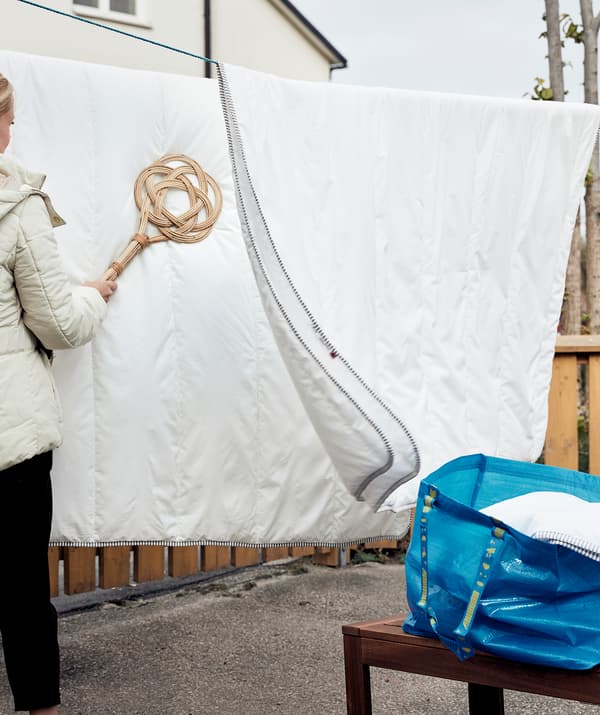 Přikrývky pověšené na šňůře, žena je vyklepává plácačkou na koberce BORSTA  