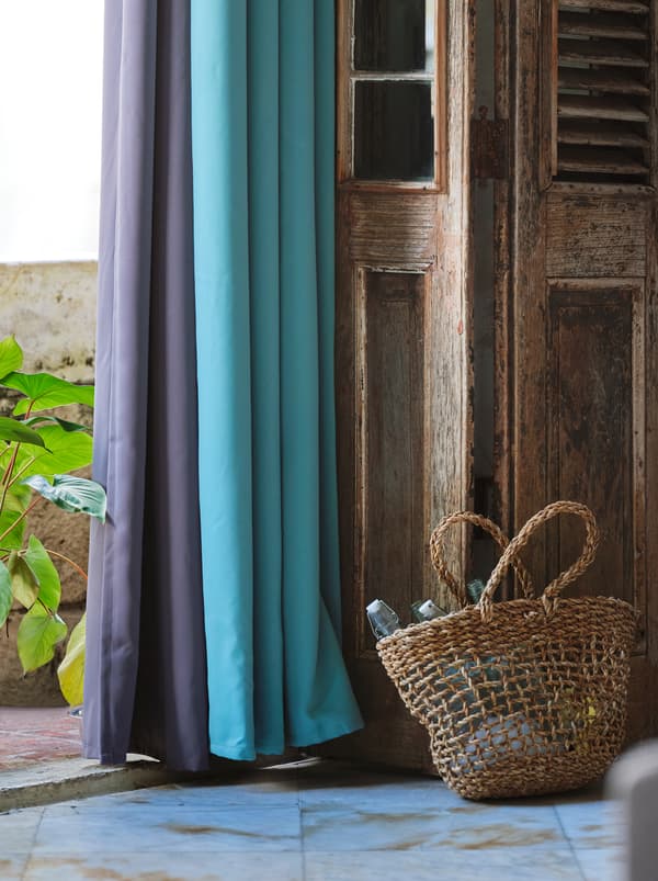 Purple and turquoise block out curtains hanging against an open, wooden door with a woven basket placed next to it.