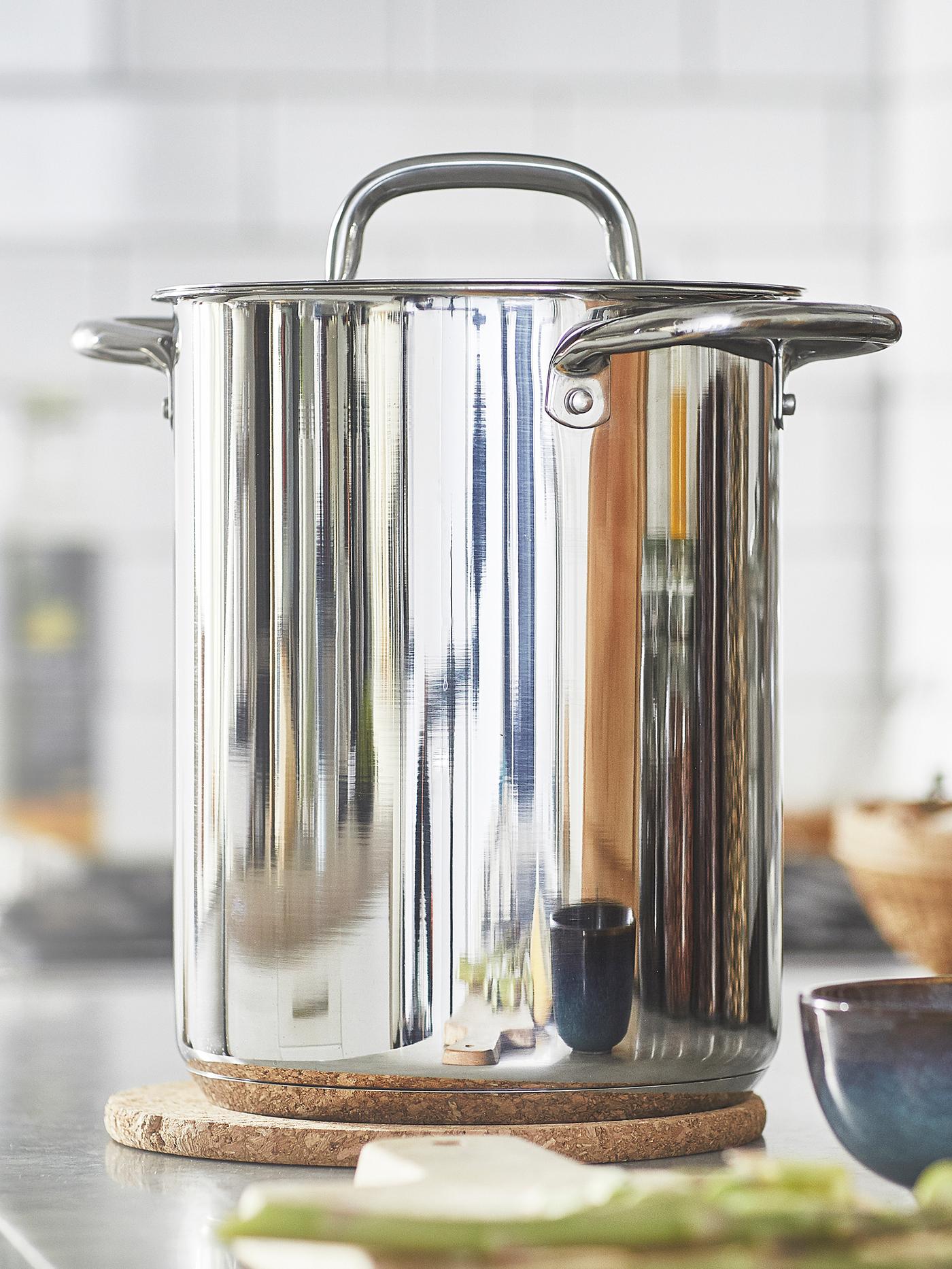 قدر مع غطاء IKEA 365 على حامل قدور HEAT على مصطبة مطبخ رمادية بجوار سلطانية زجاجية باللون الأزرق الداكن.