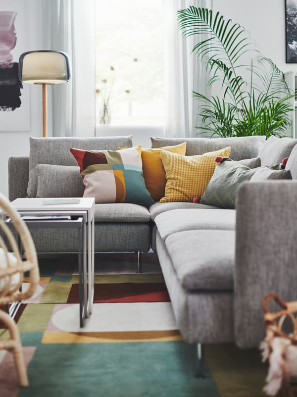 قسم من غرفة جلوس مع صوفا زاوية SÖDERHAMN رمادية على سجادة ملوّنة، وعليها مجموعة من الوسائد الملونة.