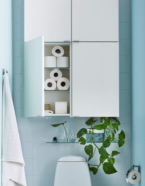 Quatre armoires blanches simples et une petite tablette en verre garnie de plantes, au-dessus d’un WC.