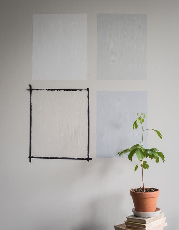 Quatre carrés peints dans des couleurs différentes sur un mur gris.