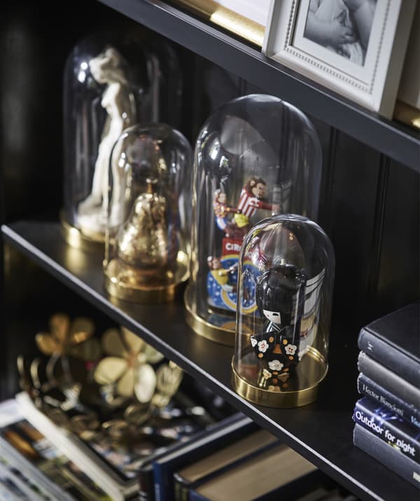 Quatre cloches en verre posées sur une tablette, abritant des bibelots et figurines.