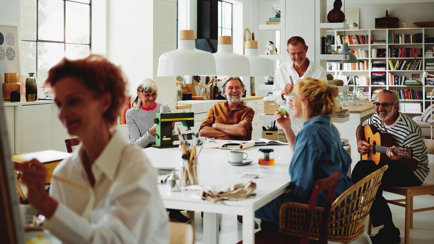 Quatre personnes autour de quatre tables MELLTORP blanches, sous trois suspensions BUNKEFLO.