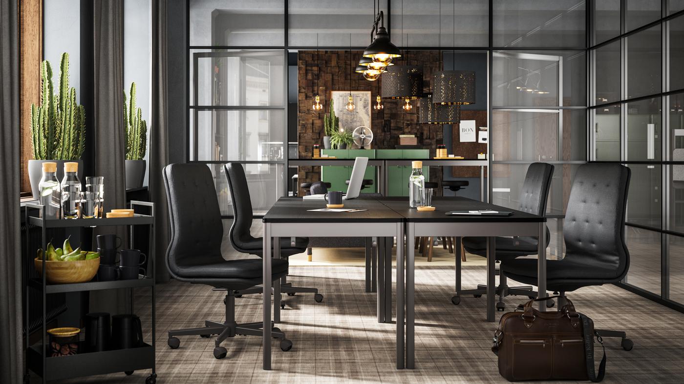 Quatre tables IDÅSEN noir/gris foncé avec chaises gris foncé dans une salle de réunion aux parois en verre.