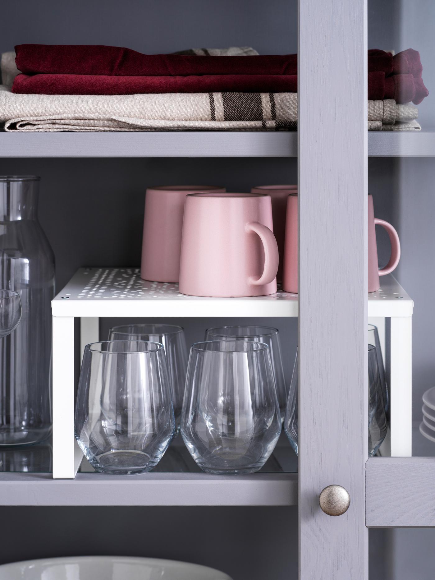 Quatre tasses roses sur une demi-étagère VARIERA blanche au-dessus de plusieurs verres dans une étagère grise.