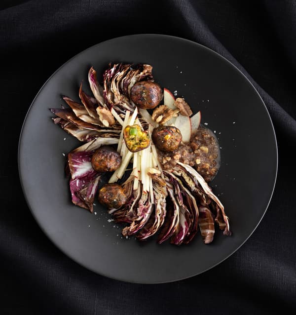 Radicchio and walnut salad with veggie balls served on a dark grey plate, seen from above.