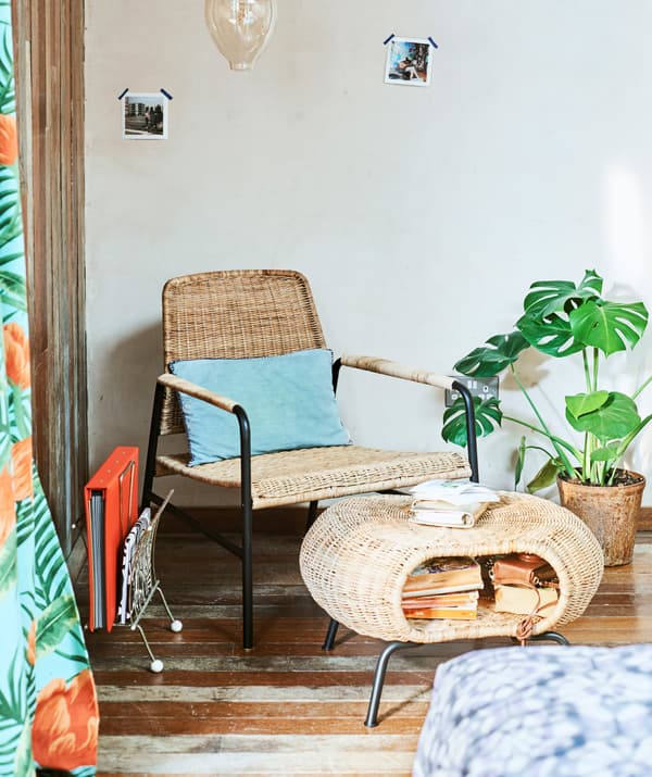 Rattan easy chair and footstool with storage space full of books in the corner of a room with decorative bulb hanging above.