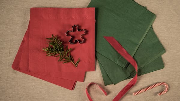 Red and green napkins, a red silk ribbon, a gingerbread man and a spruce branch. All laid out on a tablecloth. 