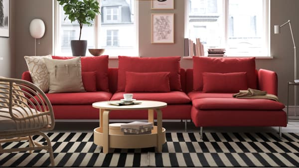Red SÖDERHAMN modular sofa in vibrant setting with striped black-and-white rug, rattan armchairs, and mix of red and green cushions.