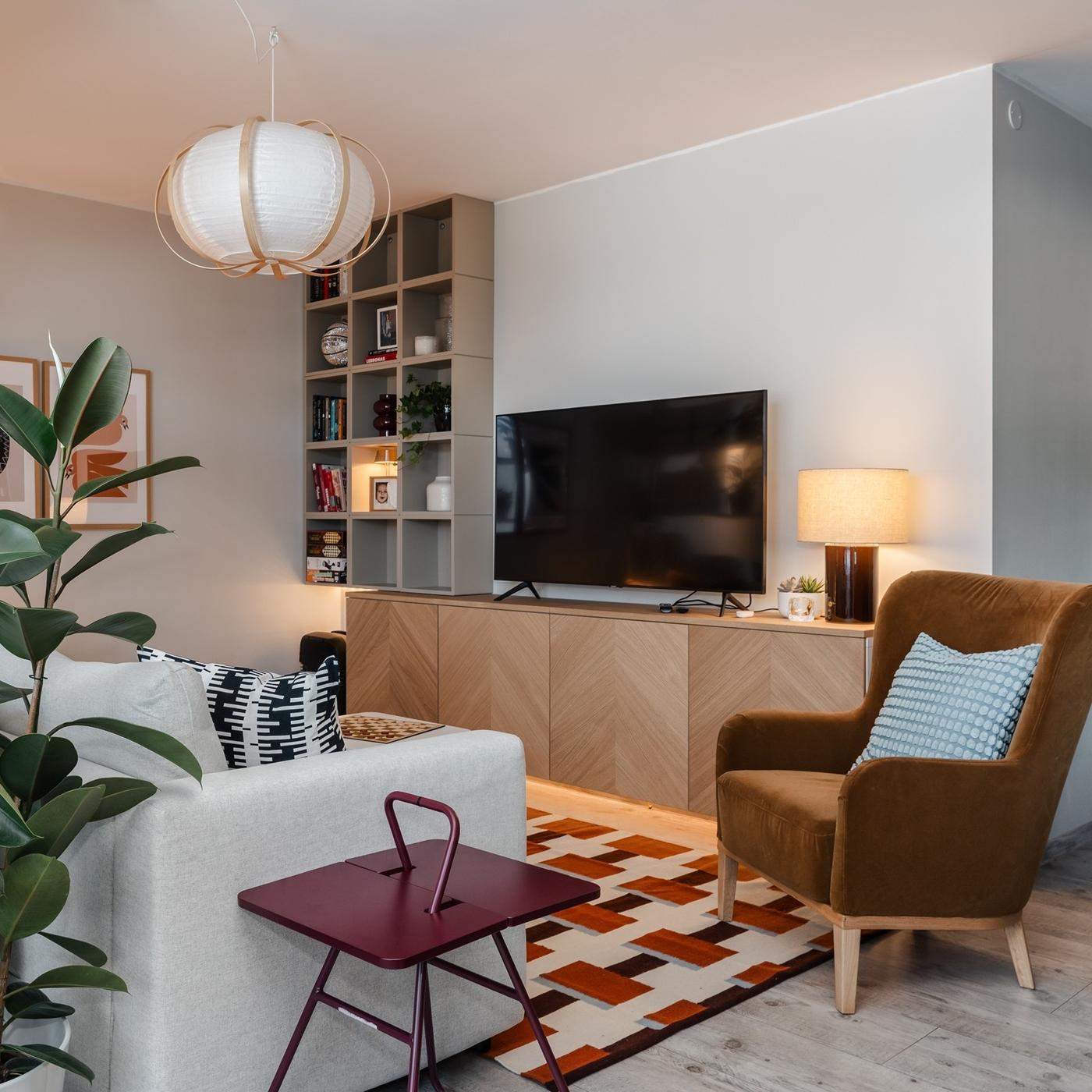 Relaxing corner with a beige sofa, warm brown armchair, TV unit, patterned rug and soft lighting.