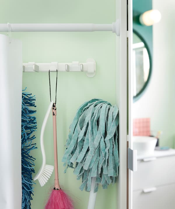 Rideau de douche employé comme cloison le long d’un mur de la salle de bains, qu’on a ouvert pour révéler une rangée d’ustensiles de ménage suspendus derrière.