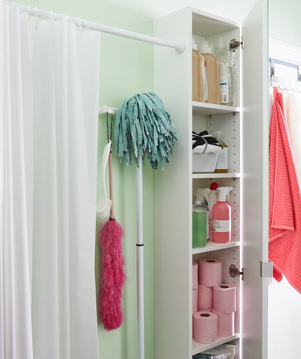 Rideau de douche installé de manière à créer une cloison le long d’un mur de la salle de bains. À côté, une armoire contenant des articles de salle de bains.