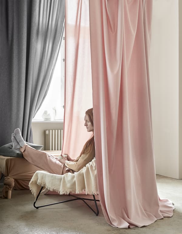 Rideaux roses et gris pendus autour d’un homme assis sur un fauteuil.