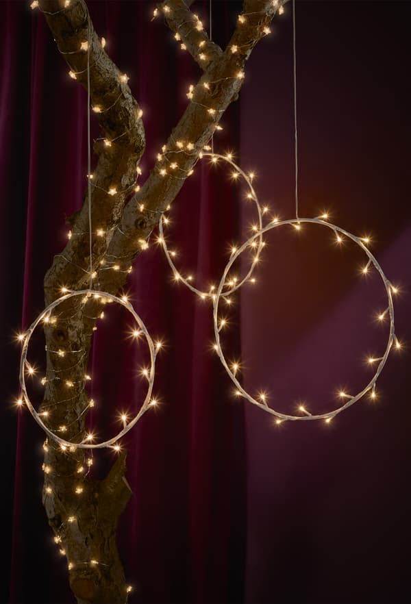Ring-shaped lamps and fairy lights wrapped around a tree branch against a dark red backdrop.