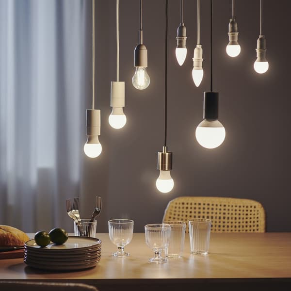 Rippuvad LED-lambipirnid, mis valgustavad söögitoas puidust söögilauda.				