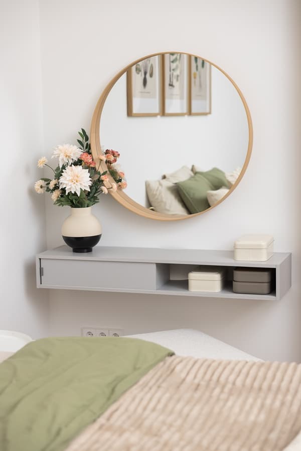 Round mirror above a wall-mounted console table with decorative items in a bedroom.