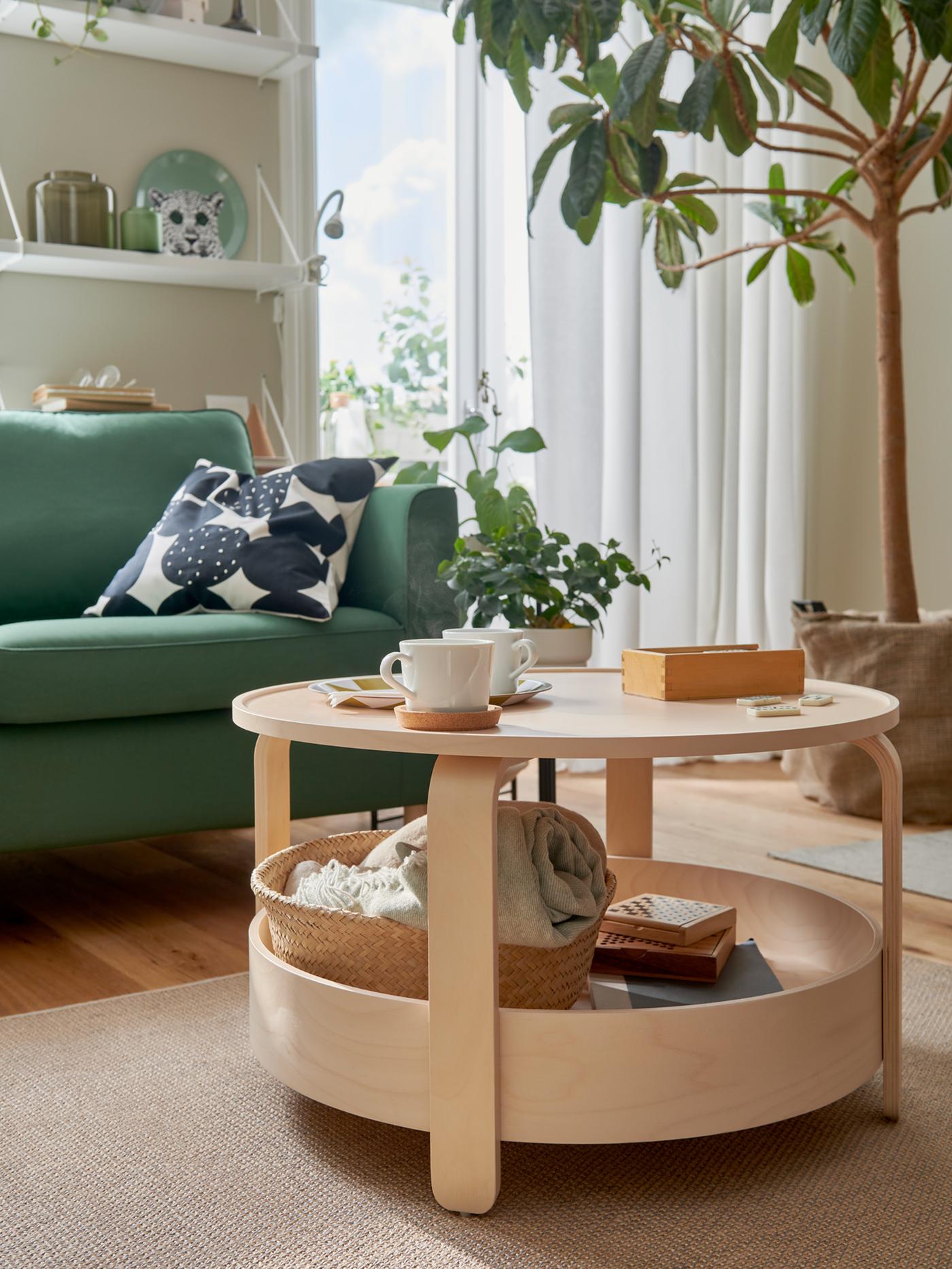 Ruang tamu yang cerah yang mempunyai meja kopi kayu birch BORGEBY, pokok berdaun lebat yang besar, sofa PÄRUP berwarna hijau gelap dan serlahan berwarna hijau yang lain.