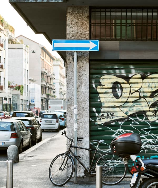 Rue en ville avec voitures et bicyclette appuyée contre un mur couvert de graffitis.