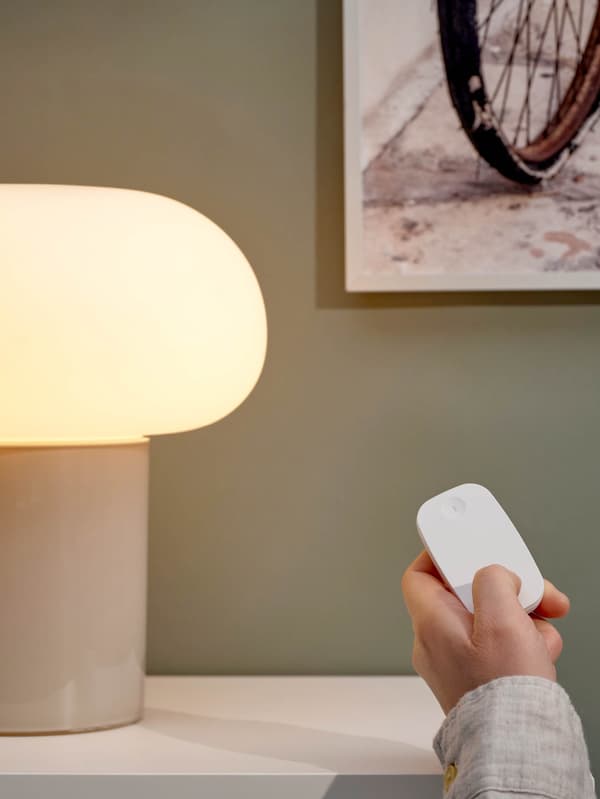 Ruka s dálkovým ovladačem TRÅDFRI rozsvěcí stolní lampu DEJSA.