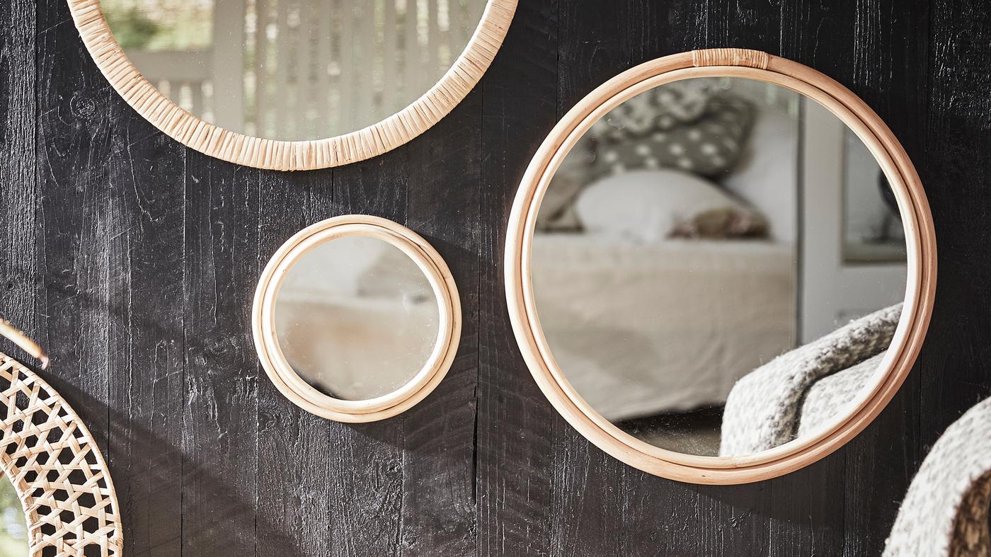 Runde Spiegel mit Rattanrahmen in verschiedenen Grössen hängen an einer Wand aus dunklem Holz.