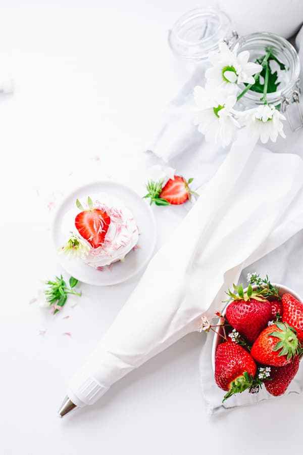 Sac à poche, ciotola di fragole e piccolo dessert con fragole su superficie bianca.