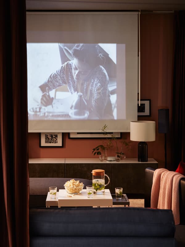 Sala de estar ambientada de cine con un proyector, un bowl con palomitas sobre una mesa de centro y un sillón gris en frente del televisor.