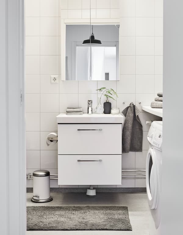 Salle de bain décorée en blanc et gris, avec serviettes propres et deux petites plantes.