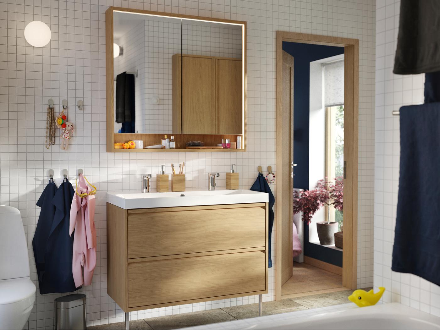 Salle de bains comprenant un meuble lavabo effet chêne avec des pieds et une armoire à pharmacie FAXÄLVEN avec éclairage intégré.