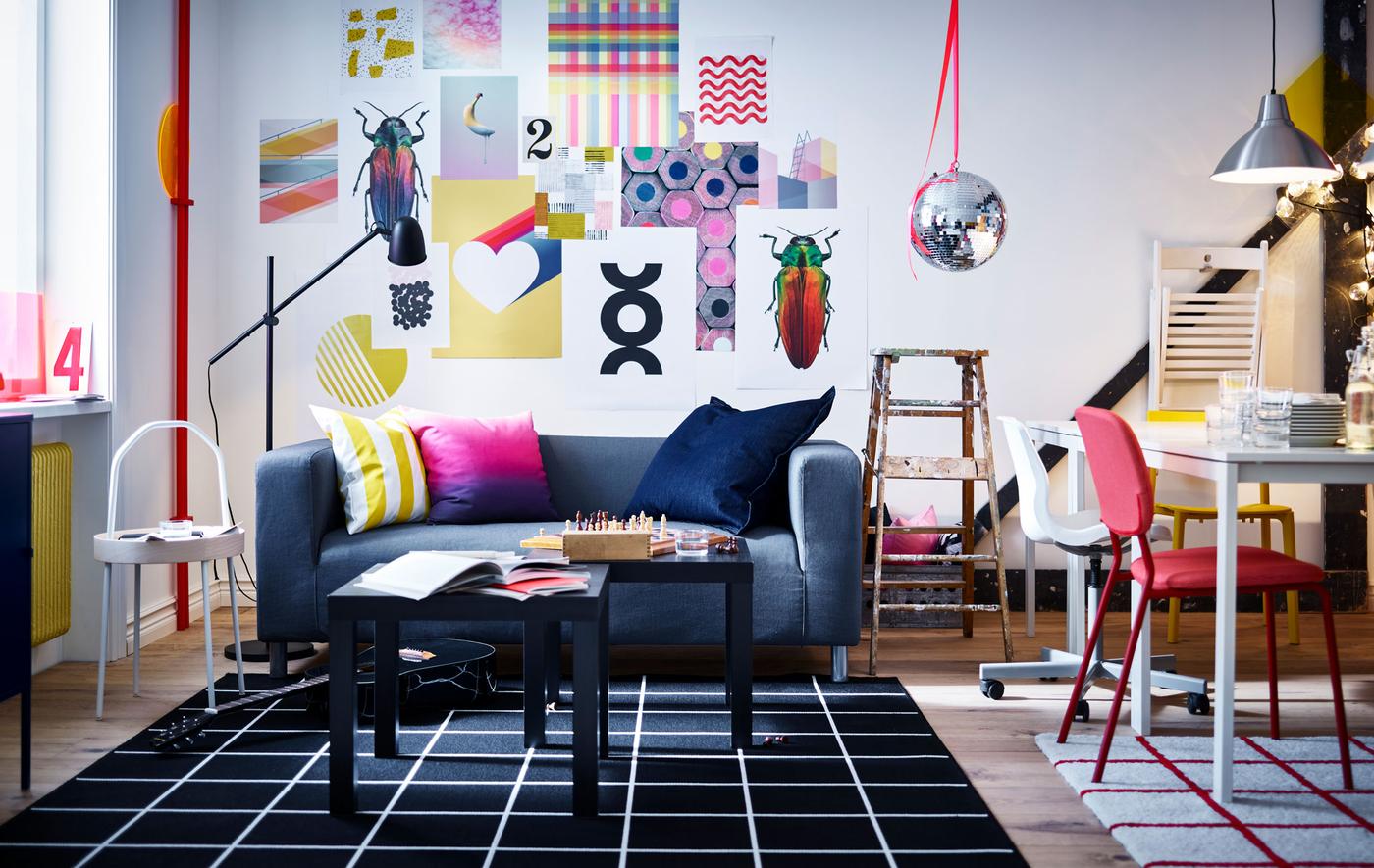 Salle de séjour et espace de travail dynamiques avec œuvres d'art sur les murs, canapé, tables basses, luminaires, tables blanches, chaises, tapis et un vieil escabeau.