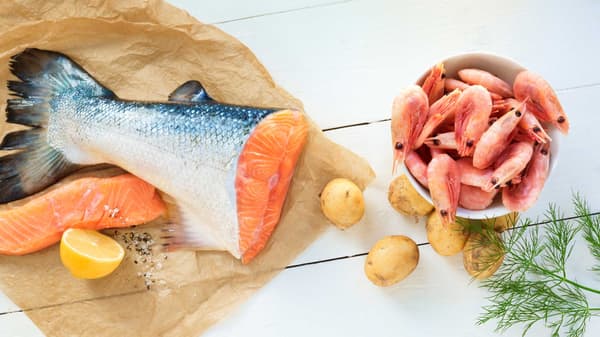 Salmon, lemons, potatoes and a bowl of shrimp are placed on a wooden table. 