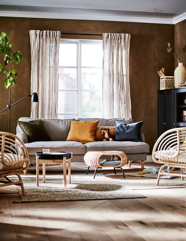 Salon dans une palette de tons terre avec des objets décoratifs, des rangements, des sièges, une table d’appoint, un repose-pieds et une plante.