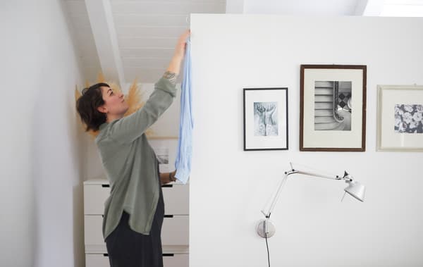 Sarah hanging a shirt behind a white wall decorated with black and white photos.