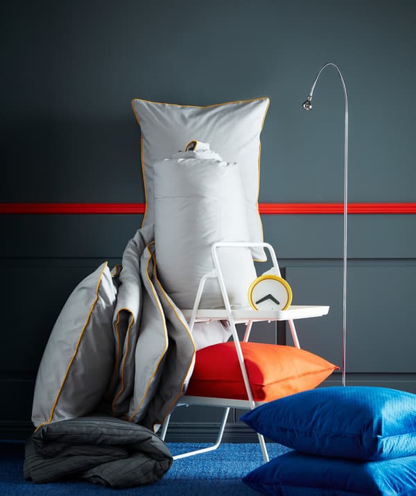 Sarung kuilt dan sarung bantal KUNGSBLOMMA IKEA berwarna kelabu dengan kelim berwarna kuning, jam penggera, lampu bacaan dan bantal berwarna jingga dan biru.