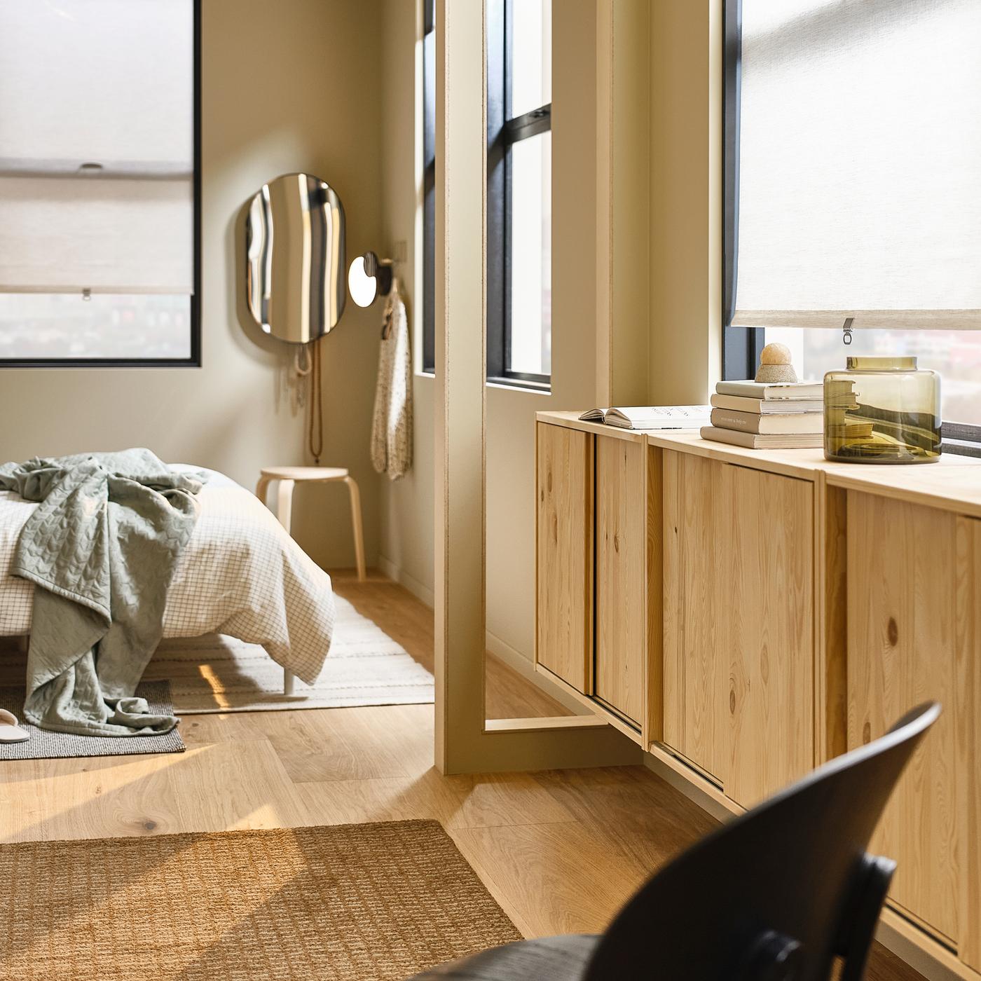 Schlafzimmer mit einem Bett und einem beigefarbenen Teppich, einem LINDBYN Spiegel und IVAR Schränken unter den Fenstern.