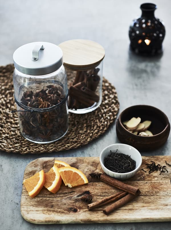 Seasonal spices in jars and cinnamon sticks and orange segments on a board.