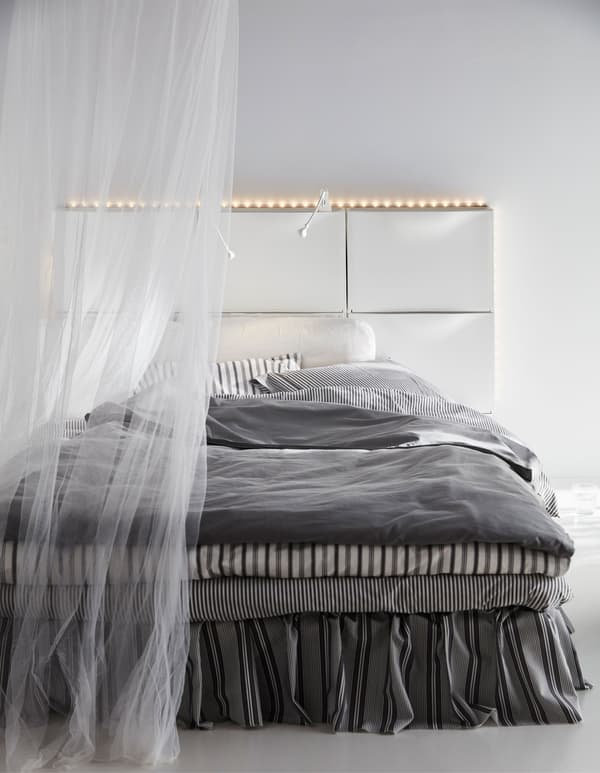Sechs IKEA TRONES Aufbewahrungen in Weiss ergeben ein Kopfteil für ein Bett.