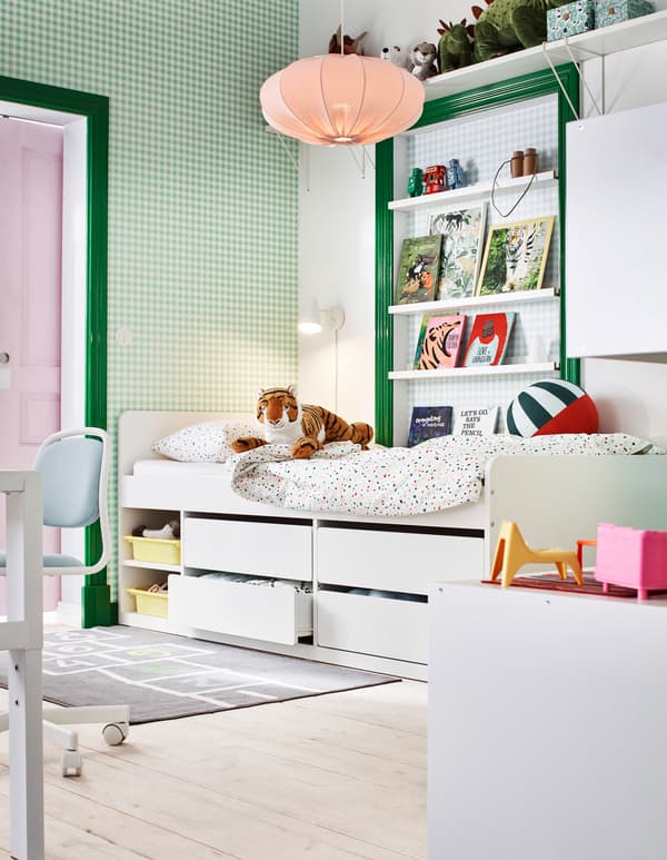 Section d’une chambre d’enfant de couleur verte et blanche, avec des livres, des jouets et un lit surélevé avec rangement sous le lit.