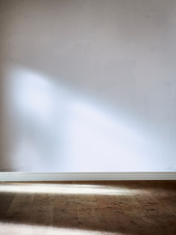 Section d’une pièce vide avec un mur blanc non peint et un plancher en bois naturel. Lumière du soleil tombant du côté.