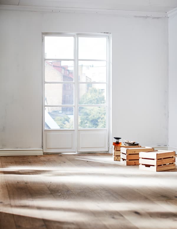 Section d’une pièce vide ensoleillée avec un mur blanc non peint et un plancher en bois naturel.