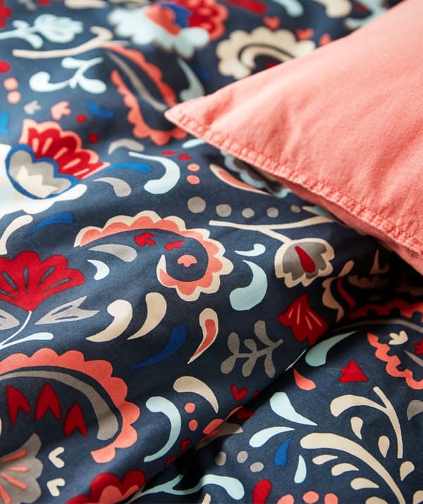 Section of a bed made with bed linen in bright colours and decorated with a traditional Swedish kurbits pattern.