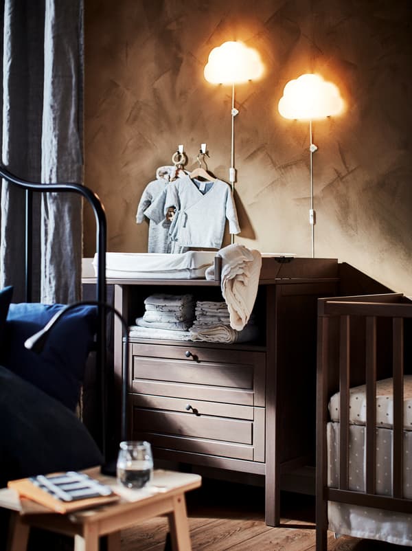 Section of a bedroom, half hidden behind a room-dividing curtain, with a baby’s cot and a SUNDVIK changing table.