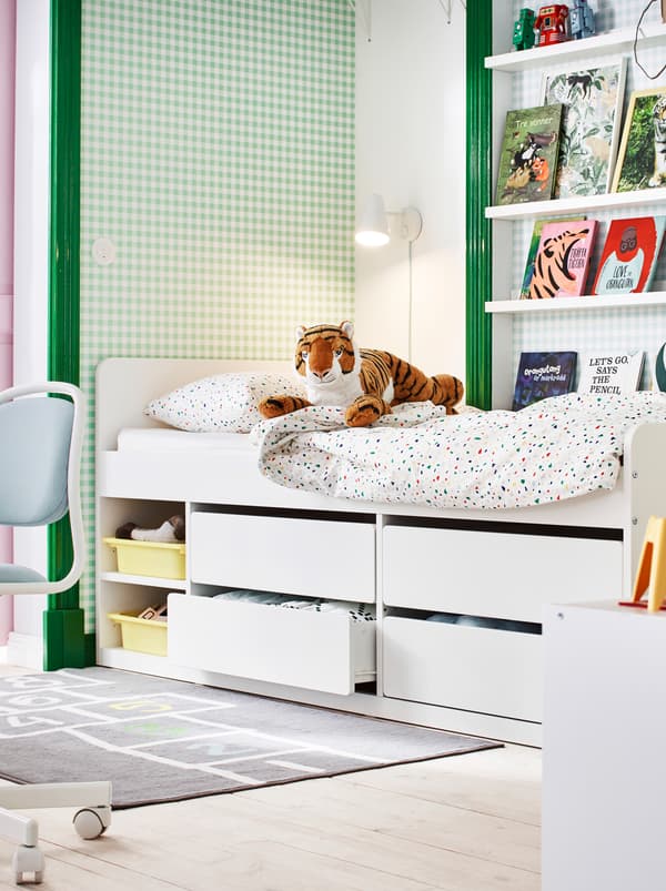 Section of a children’s room in green and white, with books on picture ledges, toys and a SLÄKT bed with under-bed storage.