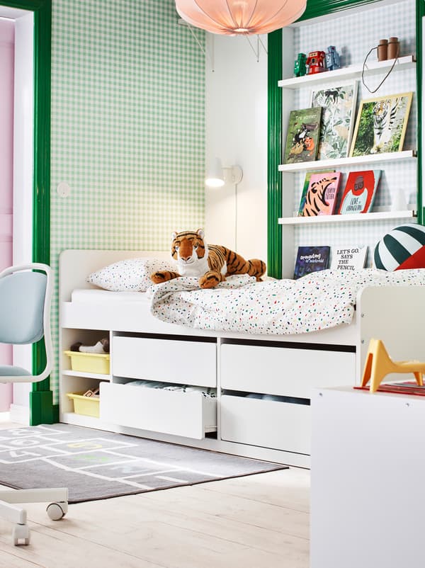 Section of a children’s room in green and white, with books on picture ledges, toys and a SLÄKT bed with under-bed storage.