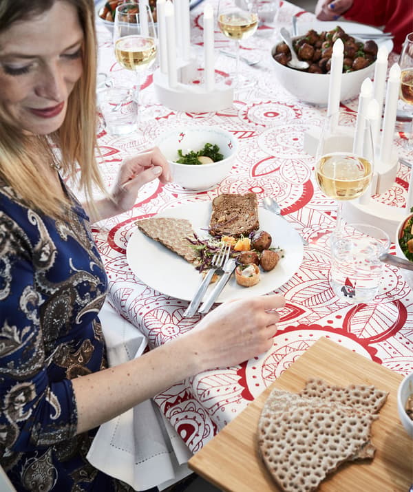 Section of decorated, festively set table with food, drinks and people. A woman is proffered a tray with crispbread.
