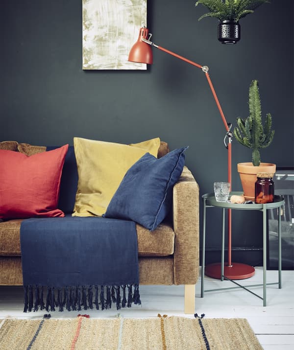 Séjour de couleur foncée avec canapé, luminaire et textiles colorés.