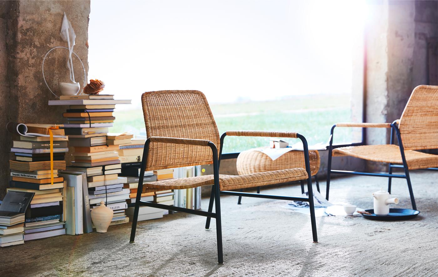 Sessel aus Rattan und Metall und ein Hocker vor einem Stapel Bücher und einem grossen Fenster