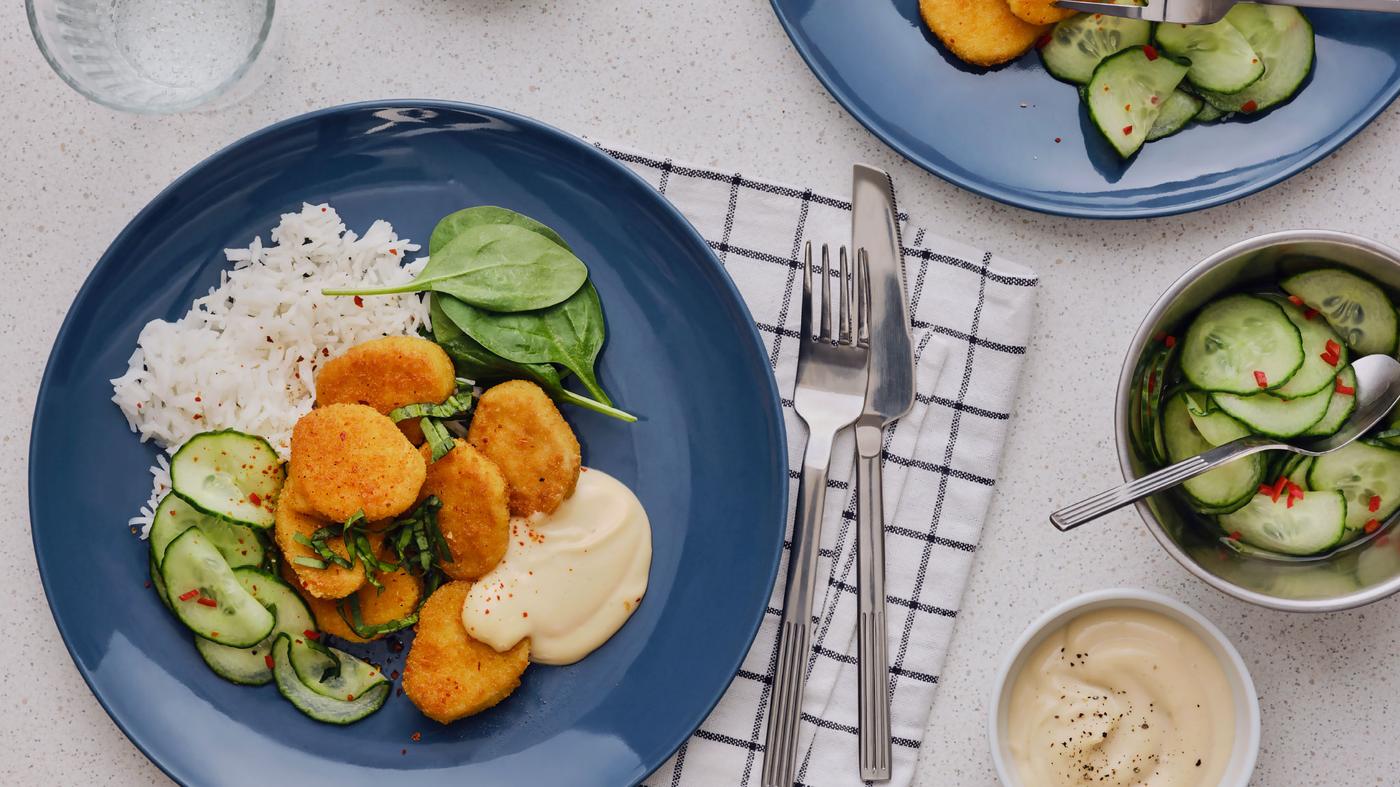 Sette bocconcini a base di frumento fritti e serviti su un piatto blu, accompagnati da riso, insalata di cetrioli e maionese al peperoncino e salsa soia.